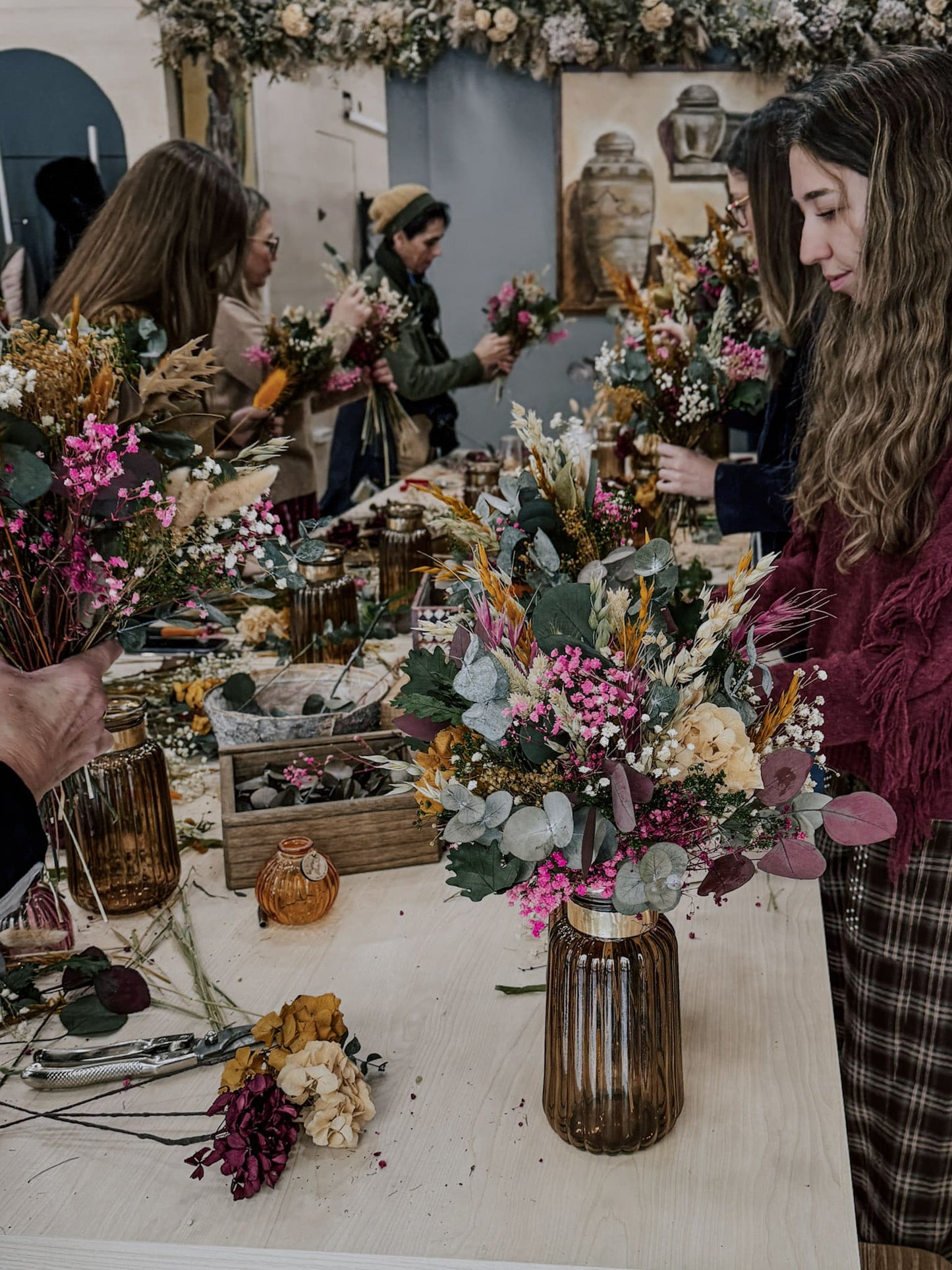 Varios asistentes realizando en el taller un ramo de flores preservadas con jarrón 