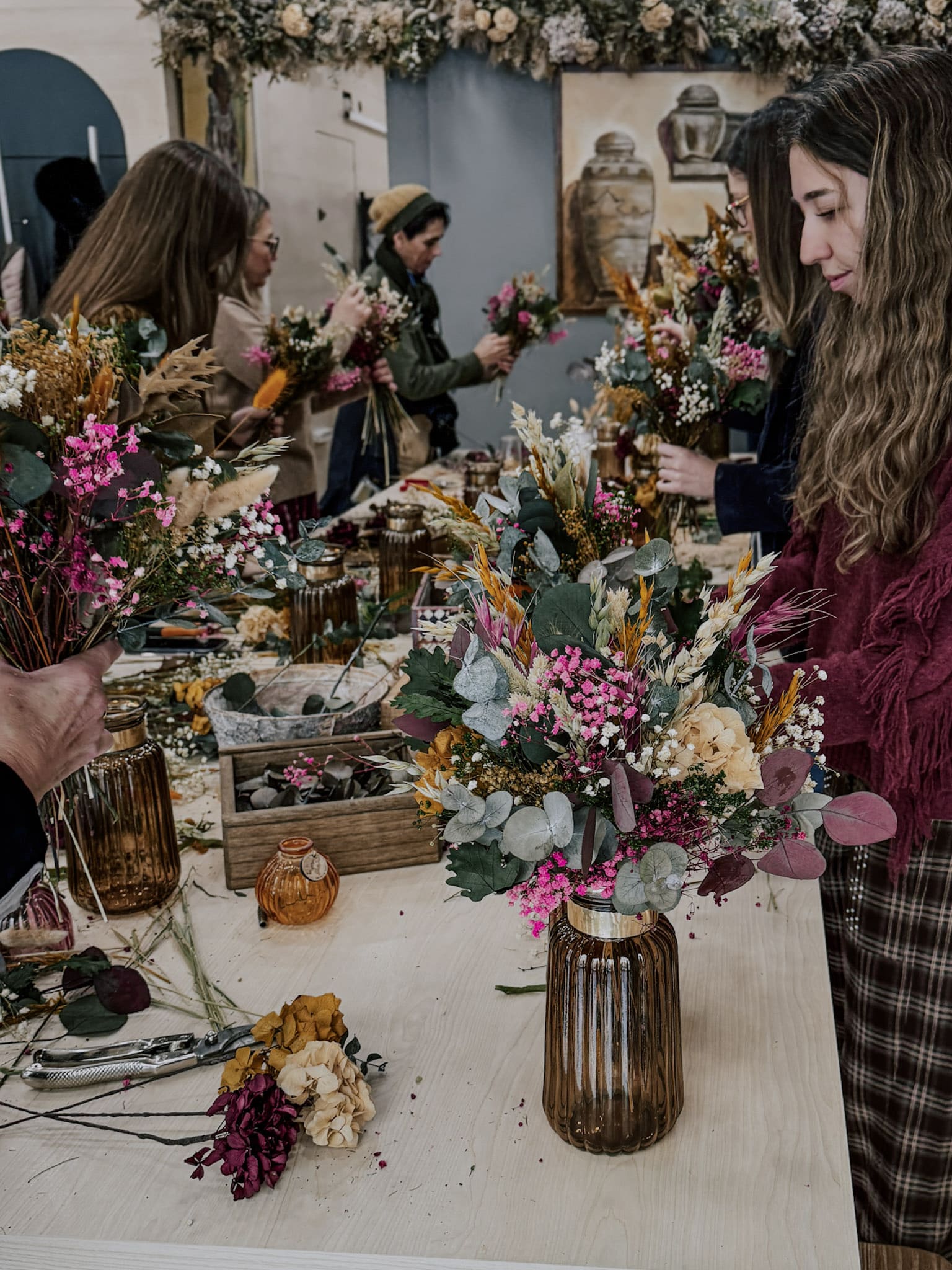 Varios asistentes realizando en el taller un ramo de flores preservadas con jarrón 